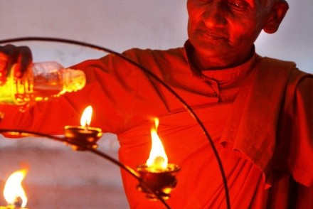 Monk lighting votive oil lamps at Kirivehera Dagoba, Kataragama, Sri Lanka